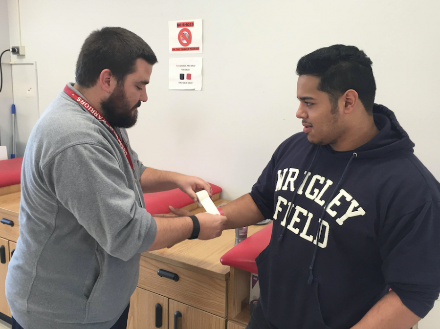 Trainer Bart Castillo helps football player Sergio Rangel wrap up his wrists before practice